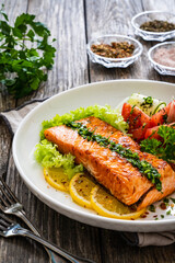 Seared salmon steak with fried potatoes and fresh vegetable salad served on wooden table
