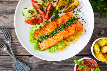 Seared salmon steak with fried potatoes and fresh vegetable salad served on wooden table
