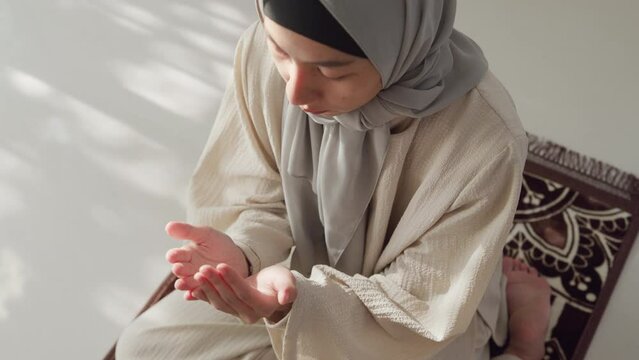 Close-up Asia muslim woman hand pray doa communicate to allah wear prayer clothes green mukena cover hijab in living room at home, pray room bright light, Islamic faith, Ramadan Kareem, Eid Mubarak.