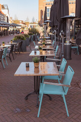 Outdoor seating area of a restaurant with teal chairs and wooden tables, still empty on a sunny day