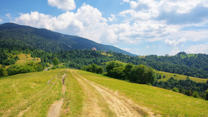 Fototapeta na wymiar rural road through green meadows on rolling hills. hiking through carpathian rural area. mountain landscape in summer on a sunny day. ridge in the distance