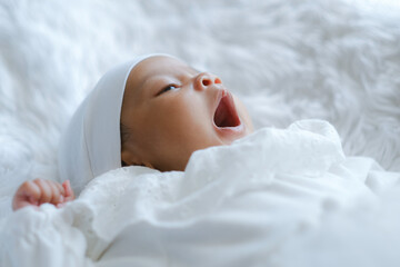 Closed up of baby yawn action, wild mouth opened and little eye open on white bed sheet.