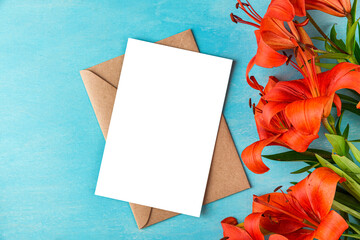 Blank greeting card with orange lily flowers on blue background. Wedding invitation. Mock up. Flat lay