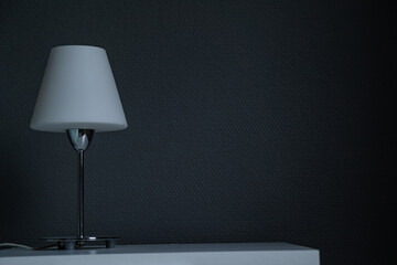 Bedside table with lamp. Dark wall. Place for text.