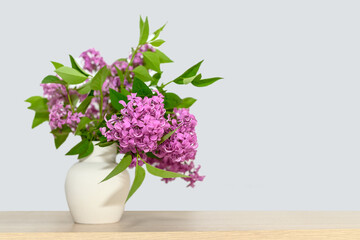 In a white gypsum vase is a bouquet of lilacs. On a wooden table.