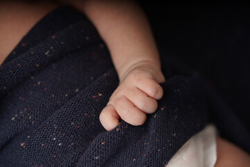 Tiny baby hands holding navy blue blanket. close-up view of the baby's cute hand the baby is laying comfortably in a blue blanket.        