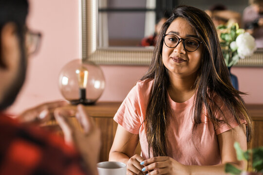 Happy couple eating breakfast and talking at dining table in morning. Indian girl and latino guy. Relationship and diversity concept
