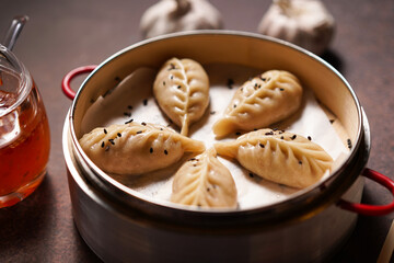 Traditional dumplings in bamboo steamer with sauces and chopsticks on dark, wooden surface with copy space, food background, dumpling steamer basket, gyoza, dimsum,  menu, oriental, fine dining