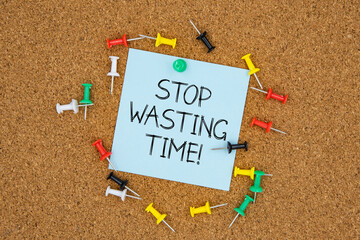 Stop wasting time text on light blue post-it paper pinned on bulletin cork board surrounding by...