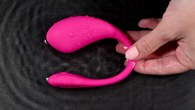 A woman is holding a pink vibrator in water. Sex toy on a black background. Generative AI