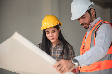 Construction worker and architects wearing hardhats and safety vests are working together at construction site ,building ,home in cooperation teamwork concept.