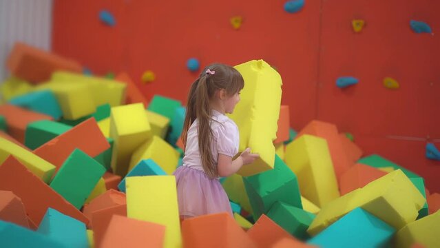 Little happy girl play and have fun in a dry pool with soft multicolored cubes in a children's entertainment center and throw paralon block in the playroom. Generative AI