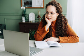 Obraz premium Contemplative Young Woman Taking Breaks from Online Learning and Working on Laptop at Home. Young Woman Studying and Working from Home, Lost in Thought and Contemplating Ideas on Her Laptop.