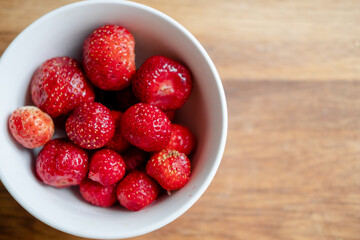 peeled and washed strawberries in a white bowl, on a wooden background, top view