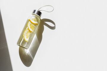 Lemon water drink detox in bottle, hard shadow at sunlight on white background. Wellness, diet,...