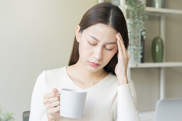 Palpitation, suffer asian young woman holding mug, drinking strong a cup of coffee, touching her chest after drink caffeine, tea while working from home, face expression stress, illness people. - obrazy, fototapety, plakaty