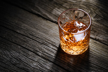 A glass of Whiskey on a rustic wooden board, that can be surface of barrel. Moody atmosphere.