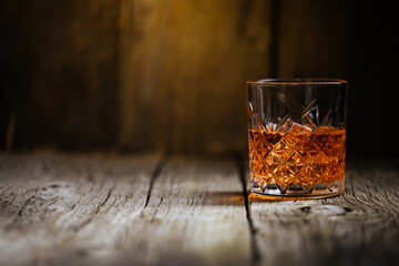 A glass of Whiskey on a rustic wooden board, that can be surface of barrel. Moody atmosphere. - obrazy, fototapety, plakaty