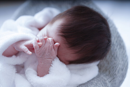Cute little baby sleeping and covering her face with hands Newborn peel. Newborn Baby with a white blanket. Close up, cute baby sleeping with hand peeling.                    