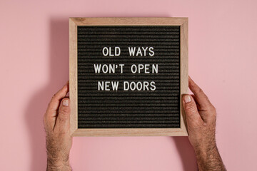Old ways will not open new doors. Motivational quote on a black letter board,y on a pink background. Inspirational quote of the day concept. Greeting card, postcard