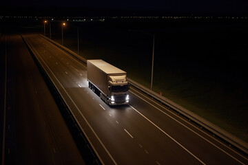 A large european semi-trailer moves along the highway at night with its headlights on. Generative AI