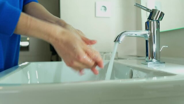 A girl in a blue medical suit washes hands. It soap with soap and carefully cleanses under the dda under the tap. Covid, Epivate. High quality FullHD footage Generative AI