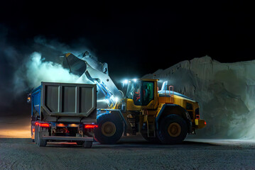 Heavy construction and mining machinery loading a dump truck with gravel in a quarry on the night...
