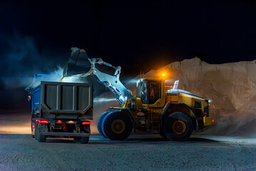 Fototapeta Heavy construction and mining machinery loading a dump truck with gravel in a quarry on the night shift. obraz