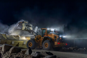 Heavy construction and mining machinery unloading gravel into silos on the night shift.