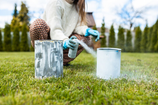 A woman paints metal cans in white color for planting plants and flowers