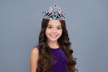 Teenage selfish girl celebrates success victory. Teen child in queen crown isolated on grey background. Princess in tiara. Prom party. Happy girl face, positive and smiling emotions.