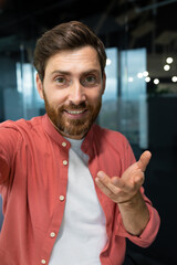 Vertical photo. Close-up photo. Young man freelancer, blogger in red shirt greets and talks to the...