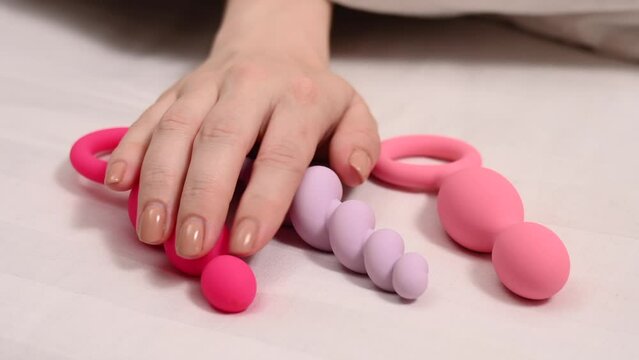 A woman chooses anal beads from a set while lying in bed.  Generative AI