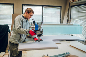 Fototapeta na wymiar Profile view of a worker using a foam cutter at his furniture workshop.
