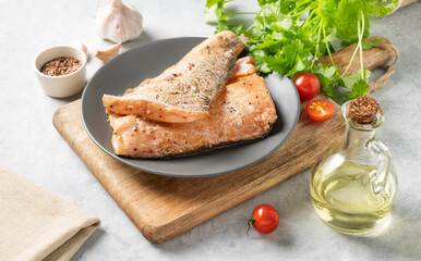 Raw salmon, greased with marinade with spices on a plate on a light background with fresh herbs and vegetables.