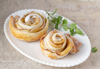 puff buns in the shape of roses with an apple and a sprig of mint on a white oval plate