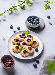 Homemade kurabye cookies with berry filling on a blue background with blueberries and jam. Healthy and delicious pastries with berries.