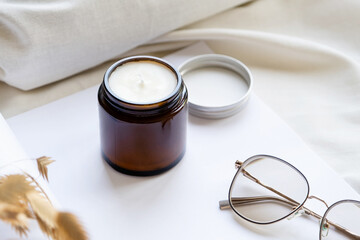 Obraz na płótnie Canvas Soy wax aroma candle in brown jar on bed , with fashion glasses. Candle mockup design