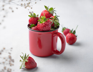 Juicy strawberries in a red cup on a light  background with flowers. Farm ripe healthy berries. Free space for text