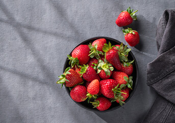 Juicy strawberries in a black bowl on a dark background with napkin. Farm ripe healthy berries. Top view