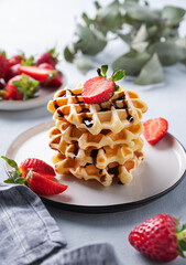 Homemade soft waffles with fresh strawberries and chocolate topping in a stack in a plate on a light background close up. Traditional Belgian waffles. Healthy  breakfast