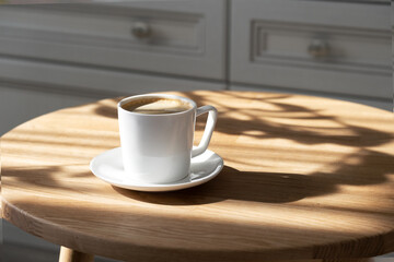 A white porcelain cup with coffee on a saucer stands on a round table