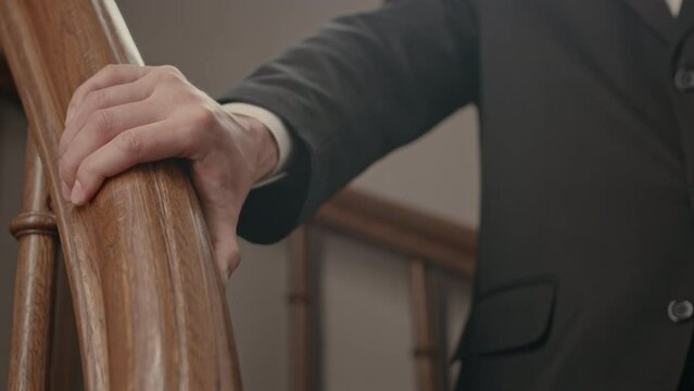 Closeup of unrecognizable Catholic priest in suit leaning his hand on wooden staircase handrail in church