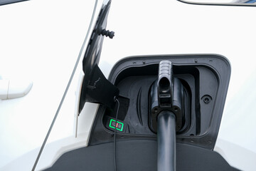 Close up charging white electric car. Electric car charging cable in jack close-up with open cover with instruction sign. Eco friendly car with electric. Seelctive focus.
