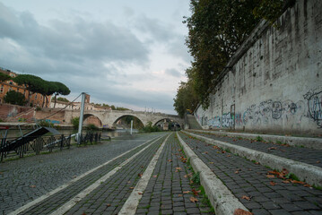 Rome, Tiber river bank, low angle, with autumn leaves and bridge in the background