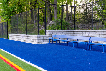 Late afternoon photo of a blue seat or bench with a synthetic turf field and retaining wall in the...