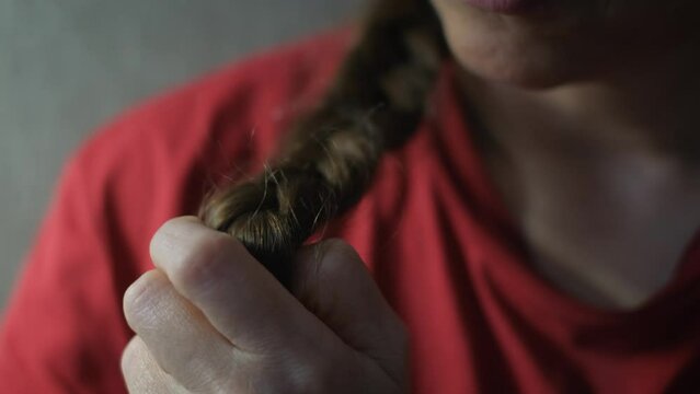 A woman pulls a braid of hair in her hands, overcoming excitement, close-up