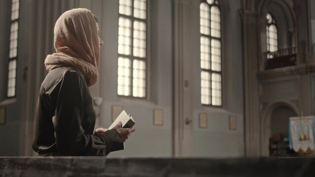 Mature Caucasian female parishioner in headscarf reading Bible in Catholic Church