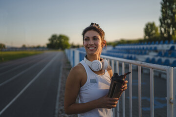 Fototapeta premium One woman stand at stadium with supplement water bottle take a brake