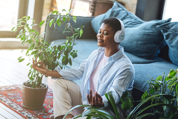 Obraz premium Young beautiful plus size woman doing yoga in living room, home meditation wearing headphones, listening to calm music, relaxing. Concept of mental health, wellbeing, relaxation, enjoyment, self care